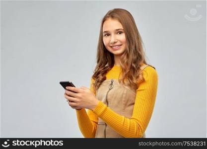 technology, communication and people concept - smiling teenage girl using smartphone over grey background. smiling teenage girl using smartphone