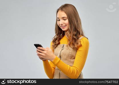 technology, communication and people concept - smiling teenage girl using smartphone over grey background. smiling teenage girl using smartphone