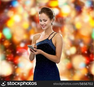 technology, communication and people concept - smiling woman in evening dress holding smartphone over red holidays lights background