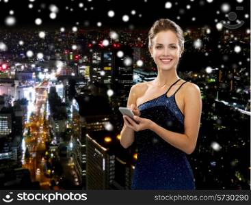 technology, communication and people concept - smiling woman in evening dress holding smartphone over snowy night city background