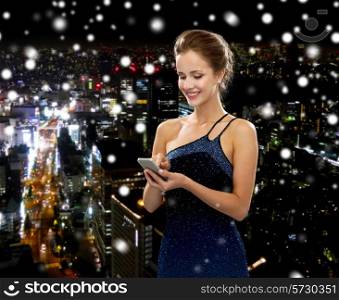 technology, communication and people concept - smiling woman in evening dress holding smartphone over snowy night city background