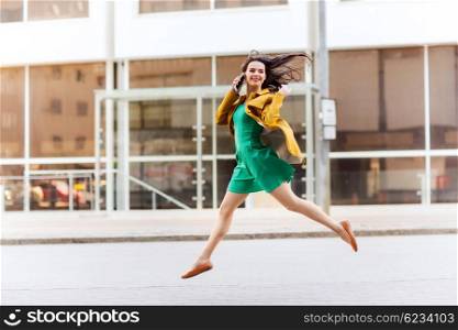 technology, communication and people concept - smiling young woman or girl calling on smartphone on city street and jumping high