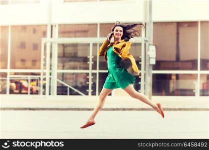 technology, communication and people concept - smiling young woman or girl calling on smartphone on city street and jumping high. smiling young woman or girl calling on smartphone