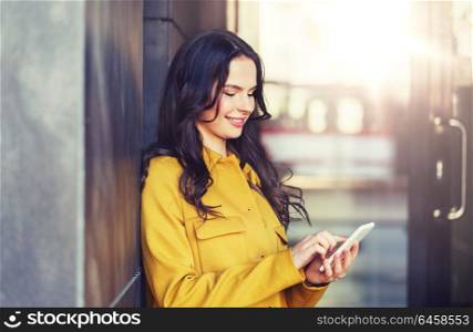 technology, communication and people concept - smiling young woman or girl texting on smartphone on city street. smiling young woman or girl texting on smartphone