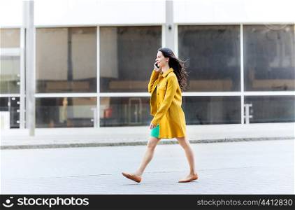 technology, communication and people concept - smiling young woman or girl walking on city street and calling on smartphone