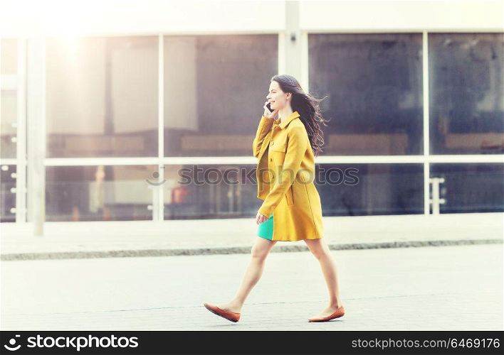 technology, communication and people concept - smiling young woman or girl walking on city street and calling on smartphone. smiling young woman or girl calling on smartphone