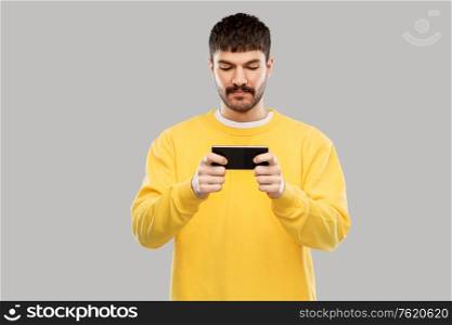 technology, communication and people concept - young man playing game on smartphone over grey background. young man playing game on smartphone
