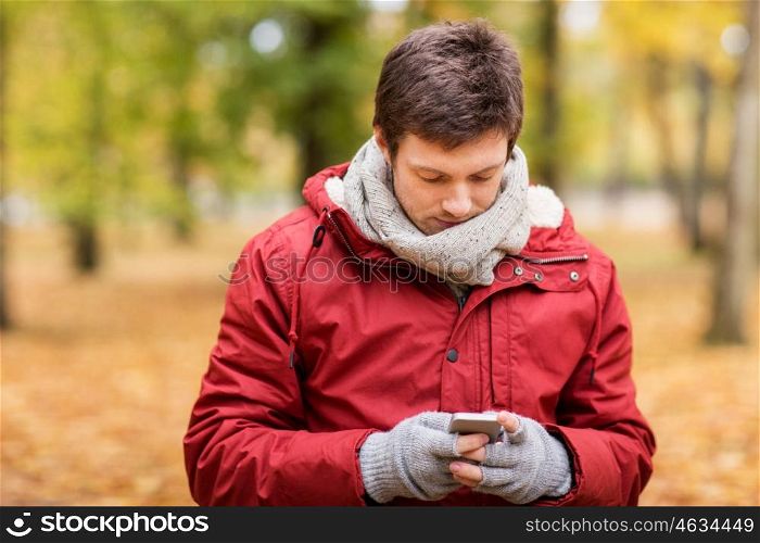 technology, communication and people concept - young man with smartphone walking at autumn park