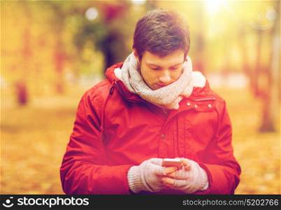 technology, communication and people concept - young man with smartphone walking at autumn park. young man with smartphone walking at autumn park