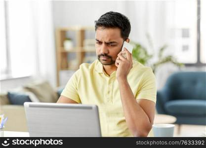 technology, communication and remote job concept - indian man calling on smartphone with laptop computer working at home office. man calling on smartphone at home office