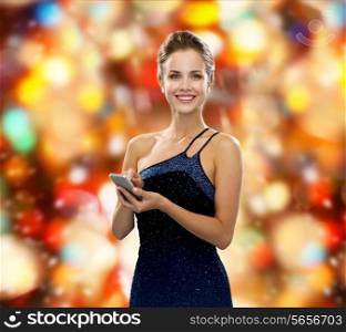 technology, communication, christmas and people concept - smiling woman in evening dress holding smartphone over red holidays lights background