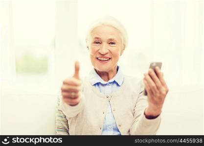 technology, communication, gesture age and people concept - happy senior woman with smartphone and showing thumbs up at home