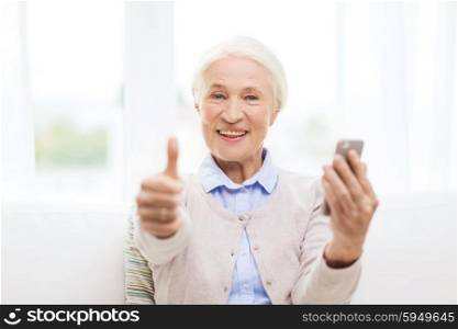 technology, communication, gesture age and people concept - happy senior woman with smartphone and showing thumbs up at home
