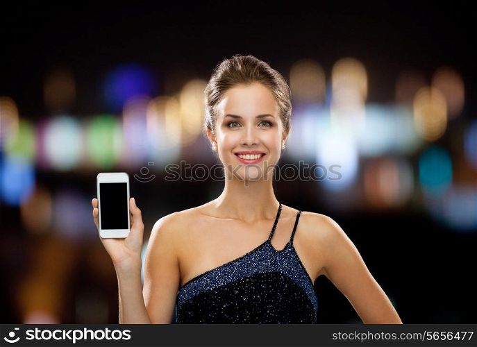 technology, communication, holidays, advertising and people concept - smiling woman in evening dress holding smartphone over night lights background