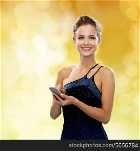technology, communication, holidays and people concept - smiling woman in evening dress holding smartphone over yellow lights background