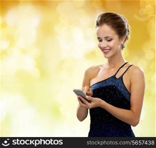technology, communication, holidays and people concept - smiling woman in evening dress holding smartphone over yellow lights background