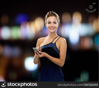 technology, communication, holidays and people concept - smiling woman in evening dress holding smartphone over night lights background