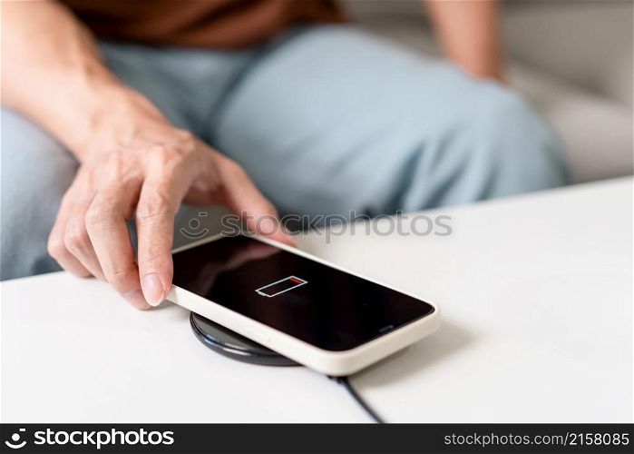 Technology Concept A person with his light blue jeans sitting on the couch and trying to charge his smartphone on the wireless battery charger.