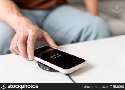 Technology Concept A person with his light blue jeans sitting on the couch and trying to charge his smartphone on the wireless battery charger.