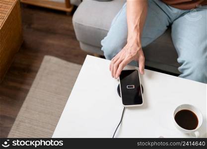 Technology Concept A person with his light blue jeans sitting on the couch and trying to charge his smartphone on the wireless battery charger.