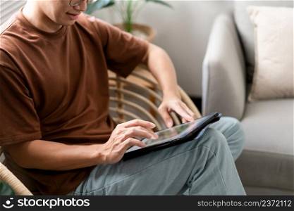 Technology Concept The male with his casual T-shirt and jeans sitting comfortably on the wooden chair and doing touchscreen for checking the web browser on the iPad.