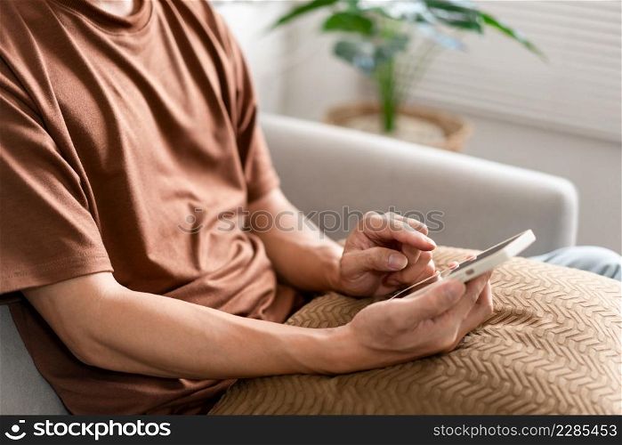 Technology Concept The man sitting next to a pot of plant, putting a small pillow on his lap, and checking something on his smartphone.
