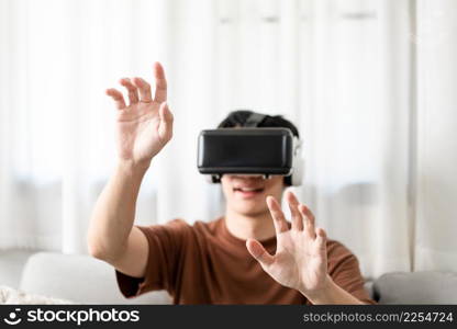 Technology Concept The man with his brown T-shirt and light blue jeans wearing a virtual reality headset while sitting on the sofa.