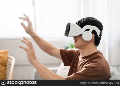 Technology Concept The man with his brown T-shirt and light blue jeans wearing a virtual reality headset while sitting on the sofa.