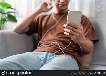 Technology Concept The person who wears glasses and headphones sitting on the grey couch and listening music on his smartphone.