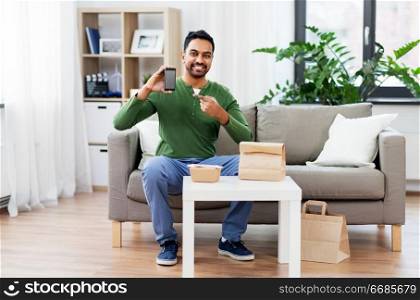 technology, consumption and people concept - smiling indian man using smartphone for food delivery at home. indian man using smartphone for food delivery