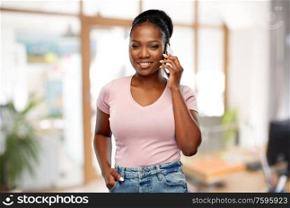 technology, corporate and people concept - happy african american woman calling on smartphone over office background. african woman calling on smartphone at office