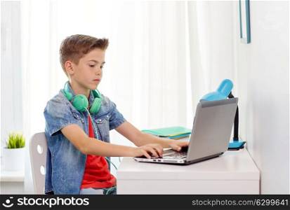 technology, cyberbullying and people concept - boy with headphones typing on laptop computer at home. boy with headphones typing on laptop at home