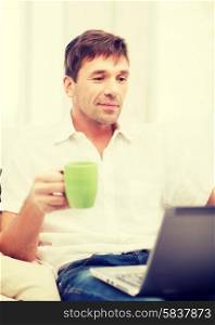 technology, drinks and lifestyle concept - man working with laptop at home, holding a cup of warm tea or coffee