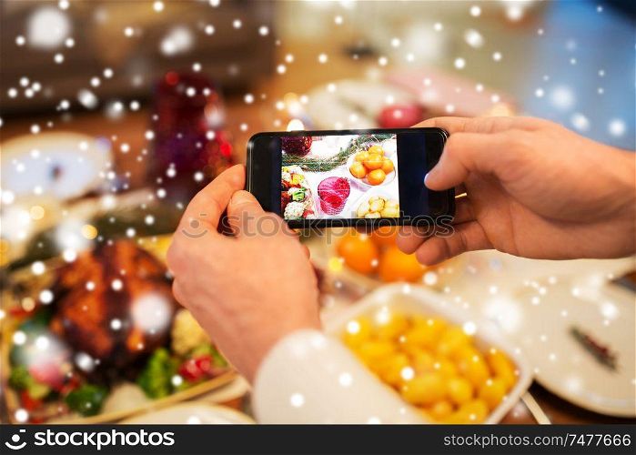 technology, eating and holidays concept - close up of male hands photographing food by smartphone at christmas dinner over snow. hands photographing food at christmas dinner