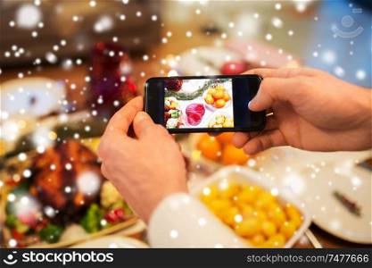 technology, eating and holidays concept - close up of male hands photographing food by smartphone at christmas dinner over snow. hands photographing food at christmas dinner