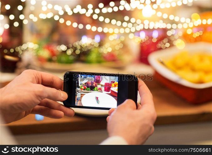 technology, eating and holidays concept - close up of male hands photographing food by smartphone at christmas dinner. hands photographing food at christmas dinner