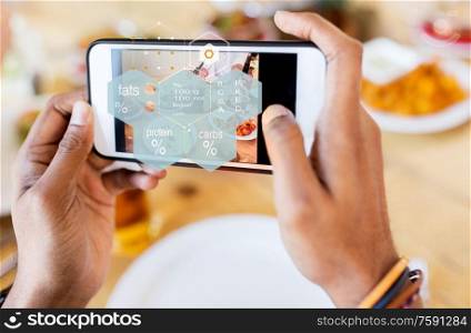 technology, eating and people concept - close up of hands with food on smartphone screen and nutritional value chart at restaurant. hands with phone and food nutritional value chart