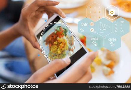 technology, eating and people concept - close up of hands with food on smartphone screen at restaurant over nutritional value chart. hands with phone and food nutritional value chart