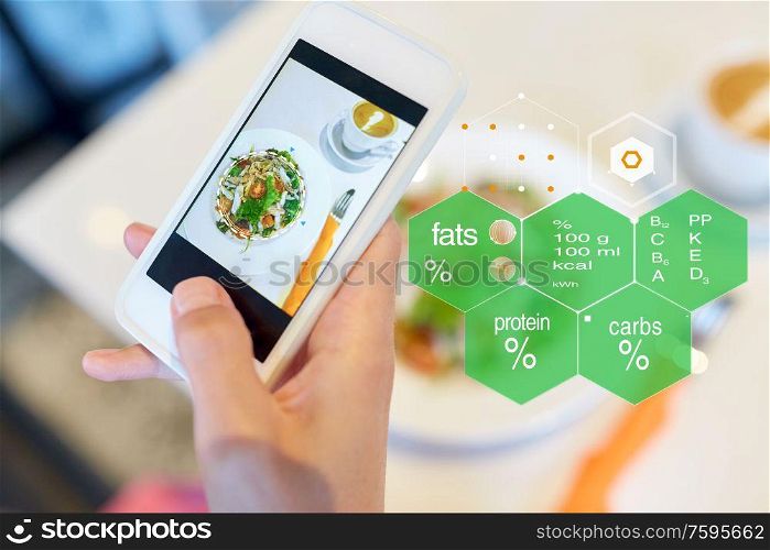technology, eating and people concept - hand with food on smartphone screen at restaurant over nutritional value chart. hand with food on smartphone screen at restaurant