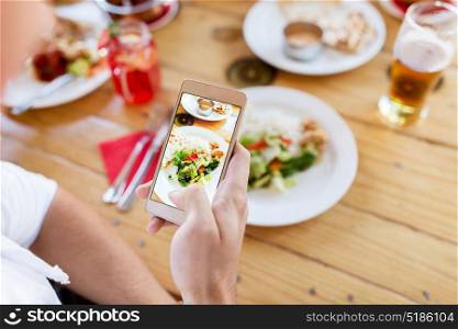 technology, eating and people concept - hand with smartphone photographing food at restaurant. hand with smartphone picturing food at restaurant