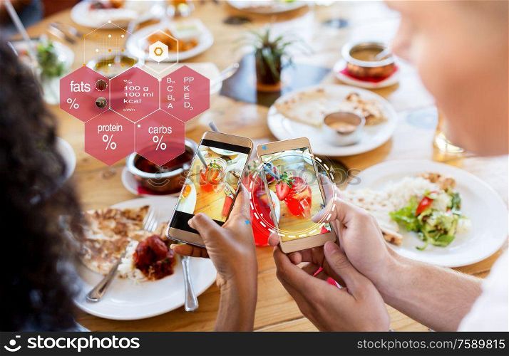 technology, eating and people concept - hands of couple with cocktail drinks in mason jar glasses on smartphone screens and nutritional value chart at restaurant. hands with phone and food nutritional value chart