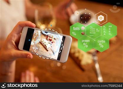 technology, eating and people concept - hands with food on smartphone screen at restaurant over nutritional value chart. hands with food on smartphone screen at restaurant