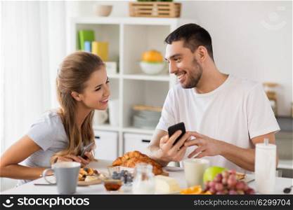 technology, eating and people concept - happy couple with smartphones having breakfast at home. couple with smartphones having breakfast at home