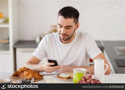technology, eating and people concept - happy man with smartphone having breakfast at home. man with smartphone having breakfast at home