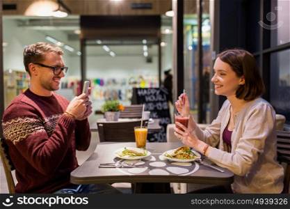 technology, eating, vegetarian food and people concept - happy couple or friends with smartphones having dinner at vegan restaurant. happy couple having dinner at vegan restaurant