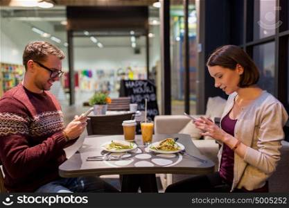 technology, eating, vegetarian food and people concept - happy couple or friends with smartphones having dinner at vegan restaurant. happy couple with smartphones at vegan restaurant