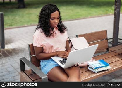 technology, education and people concept - african american student girl with laptop computer and books in city. african student girl with laptop and books in city