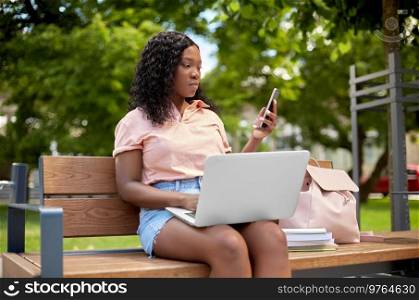 technology, education and people concept - african american student girl with laptop computer, smartphone and books in city. african student girl with laptop and smartphone