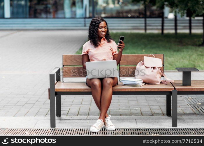 technology, education and people concept - happy smiling african american student girl with laptop computer, smartphone and books in city. african student girl with laptop and smartphone
