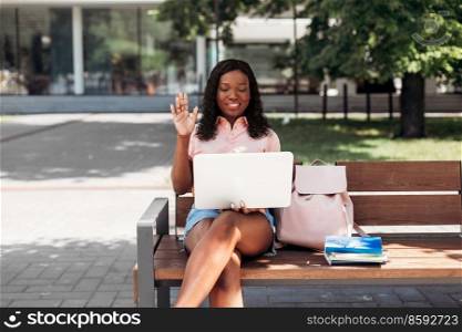 technology, education and people concept - happy smiling african american student girl with laptop compute having video call in city. african student girl with laptop having video call